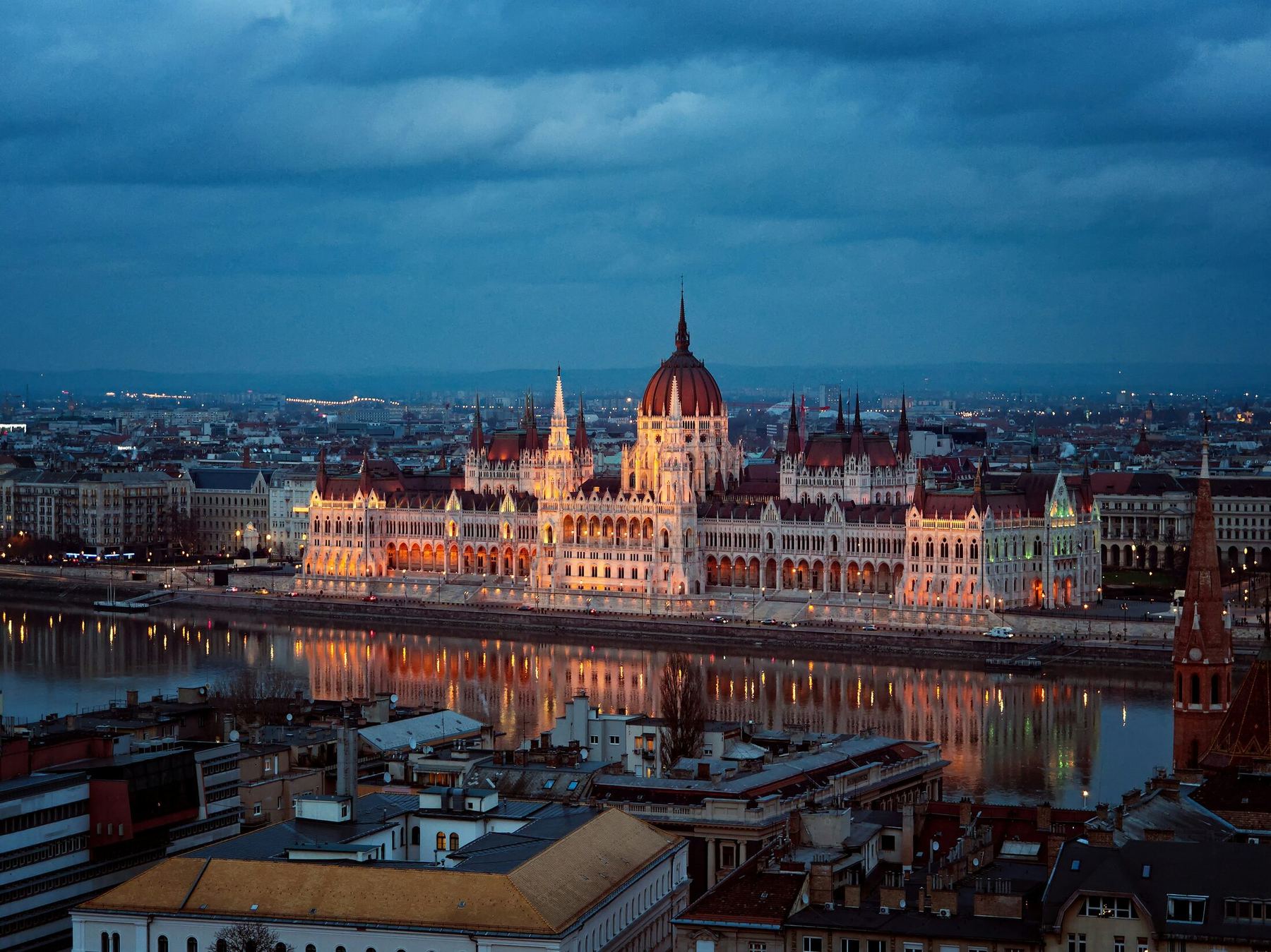Parlamento de Budapeste iluminado às margens do Rio Danúbio ao anoitecer